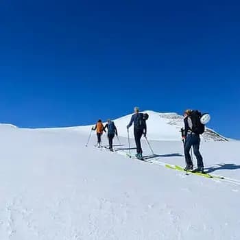 Un groupe en train de pratiquer du ski de randonnée se déplçant dans la neige en direction du sommet au loin.